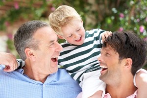 Grandfather And Father Giving Grandson Ride On Shoulders